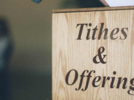 A hand placing an envelope in a tithes and offering box