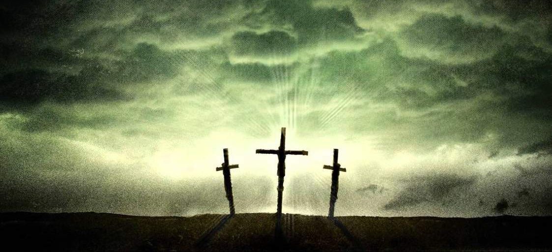Three crosses silhouetted on a hillside with light breaking through storm clouds behind them